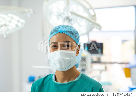 African American woman standing in hospital operating room, featuring surgical lights and monitors 128741434