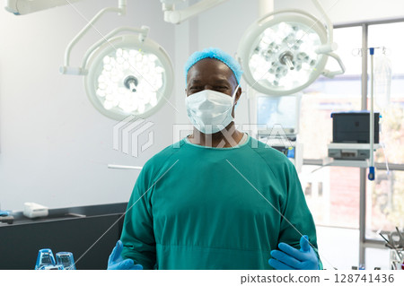 Mature African American surgeon standing in operating room, with lights, monitors and IV stand 128741436