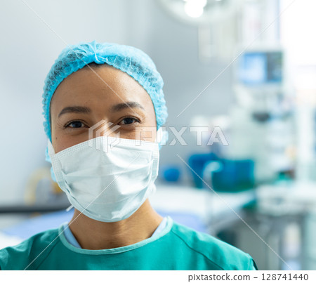 Mid adult African American woman standing in operating room, wearing green scrubs, cap and mask 128741440