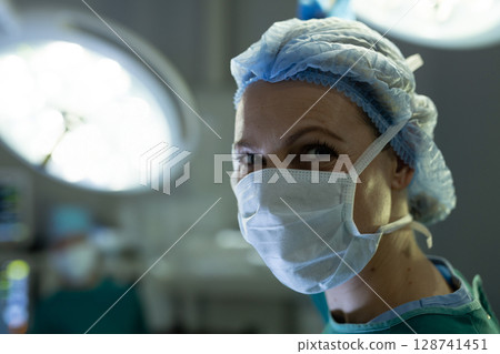 female surgeon smiling with eyes in operating room, with mask and overhead LED lights, copy space 128741451