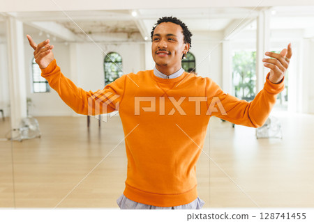 Man practicing dance moves in dance studio, using mirror panels and wooden ballet barre 128741455