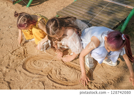 A group of children draws hearts on the sand of a beach by the ocean 128742080