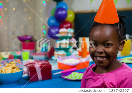 African American boy sitting at birthday party table, wearing party hat near cupcakes, copy space 128742207