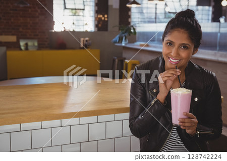 Indian man leaning against wood bar in cafe, sipping pink milkshake with whipped cream, copy space Indian man leaning against wood bar in cafe, sipping pink milkshake with whipped cream, copy space 128742224