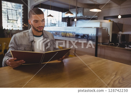 Man reading menu while sitting at wooden table in modern cafe, with pendant lights, copy space Man reading menu while sitting at wooden table in modern cafe, with pendant lights, copy space 128742230