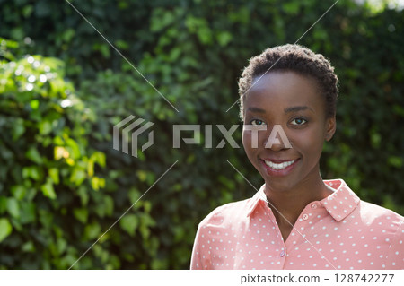 African American woman standing in front of ivy wall, wearing blouse and smiling, copy space 128742277