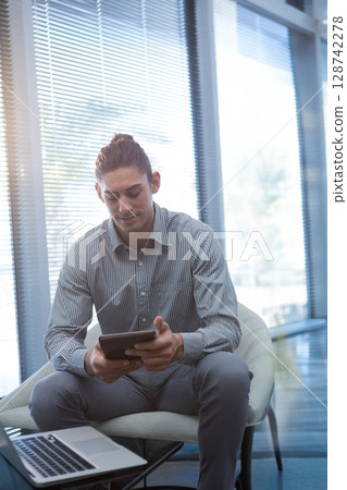 man sitting in modern corporate lounge holding tablet and viewing open laptop on glass coffee table man sitting in modern corporate lounge holding tablet and viewing open laptop on glass coffee table 128742278