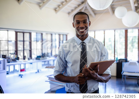 African American man smiling and holding notebook in open office, with computers and lanterns 128742305