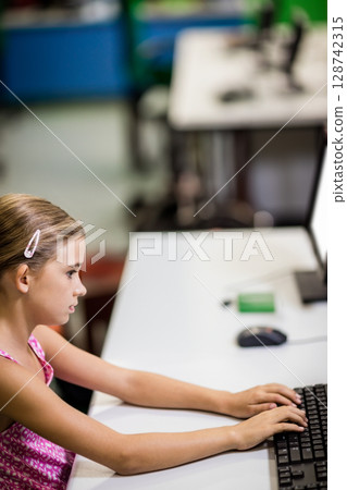 African American teenage girl typing on keyboard beside monitor in school computer lab, copy space 128742315