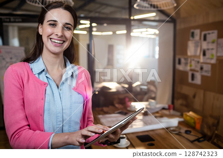 Woman interacting with tablet at wooden conference table in office, with papers and coffee cups 128742323