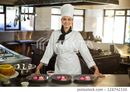 Young adult female chef showing desserts on counter in restaurant kitchen, showcasing raspberries 128742330