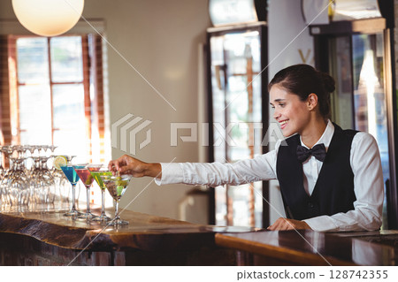 female bartender arranging cocktails behind wooden counter in bar, with martini glasses, copy space 128742355