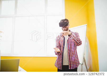 Man standing in bright yellow training room using VR headset, referencing laptop and whiteboard Man standing in bright yellow training room using VR headset, referencing laptop and whiteboard 128742372