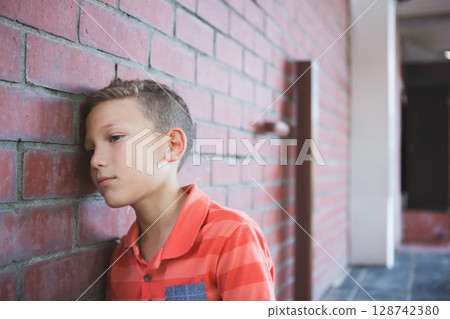 8-year-old boy leaning head on red brick wall in covered corridor with white columns, copy space 128742380