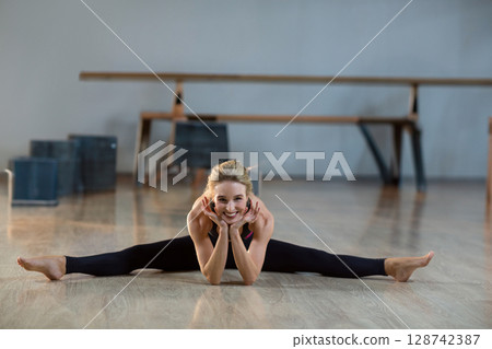 woman dancer performing straddle split in dance studio, with plyometric boxes and wooden bench 128742387