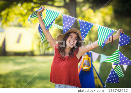 Young woman raising triangular flags in backyard garden, with blue play tent and yellow lantern 128742412