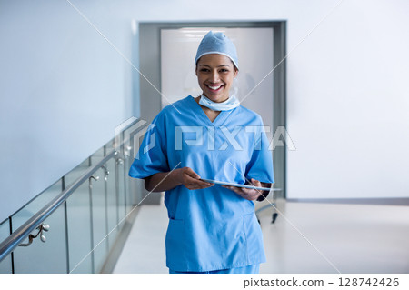 bi-racial young nurse standing in bright hospital corridor, holding tablet and smiling 128742426