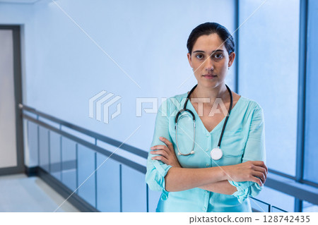 Woman doctor standing in hospital corridor, wearing teal scrubs with stethoscope, copy space 128742435