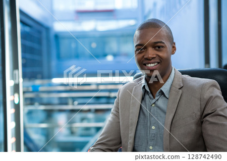 African American man sitting in chair at glass window in office viewing cityscape, copy space 128742490