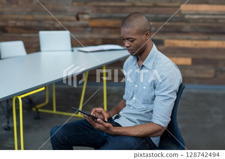 African American man sitting in meeting room, using tablet at table with notebook, copy space African American man sitting in meeting room, using tablet at table with notebook, copy space 128742494