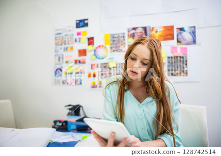 Woman reviewing design on tablet in modern creative studio, surrounded by papers and color swatches Woman reviewing design on tablet in modern creative studio, surrounded by papers and color swatches 128742514