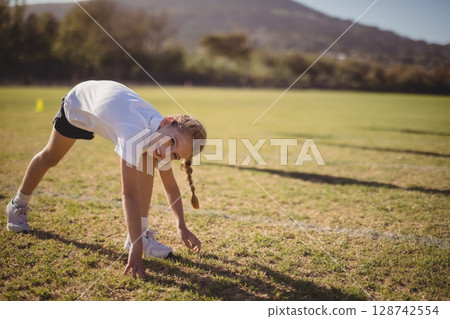 child bending down touching grass on sports field with yellow training cone nearby, copy space child bending down touching grass on sports field with yellow training cone nearby, copy space 128742554
