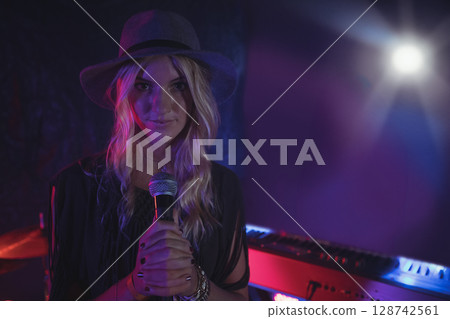 Female singer performing on indoor stage in small music venue, with microphone and keyboard Female singer performing on indoor stage in small music venue, with microphone and keyboard 128742561