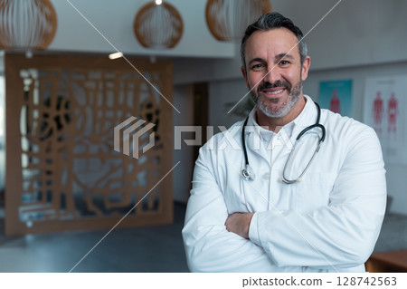 Middle-aged male doctor standing in clinic reception, wearing lab coat with stethoscope, copy space Middle-aged male doctor standing in clinic reception, wearing lab coat with stethoscope, copy space 128742563