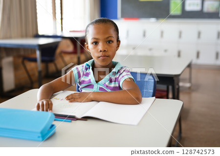 African American child studying at desk in elementary classroom, with open workbook and blue folder 128742573
