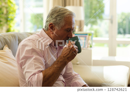 Senior man sipping from teal ceramic mug sitting on sofa in living room, copy space Senior man sipping from teal ceramic mug sitting on sofa in living room, copy space 128742621