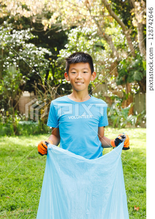 Asian child holding light blue trash bag in backyard wearing VOLUNTEER T-shirt and orange gloves Asian child holding light blue trash bag in backyard wearing VOLUNTEER T-shirt and orange gloves 128742646