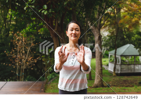 Mid adult Asian woman practicing tai chi on wooden deck in backyard, with white gazebo background 128742649