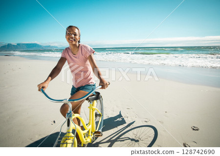 African American woman riding yellow cruiser bicycle on sandy beach, smiling against ocean waves 128742690