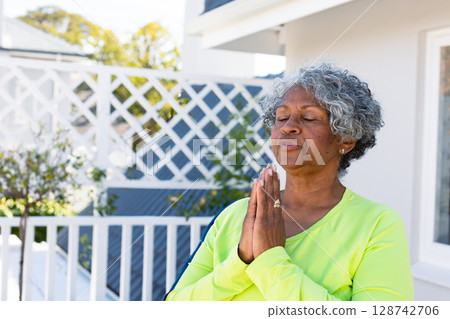 Senior woman standing on white balcony outdoors, holding hands in prayer pose and wearing gold ring Senior woman standing on white balcony outdoors, holding hands in prayer pose and wearing gold ring 128742706