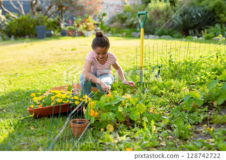 Little girl tending green plants and yellow flowers in backyard garden, using gardening fork Little girl tending green plants and yellow flowers in backyard garden, using gardening fork 128742722