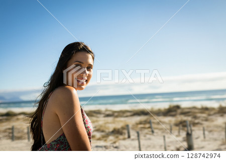 woman standing on sandy coastal dune, smiling over shoulder toward camera, copy space 128742974