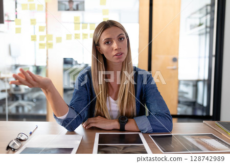 Woman sitting in modern office meeting room reviewing documents on tablet, with eyeglasses and pen Woman sitting in modern office meeting room reviewing documents on tablet, with eyeglasses and pen 128742989