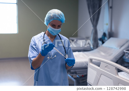 Female nurse drawing medication into syringe in hospital room, with stethoscope and vial 128742998