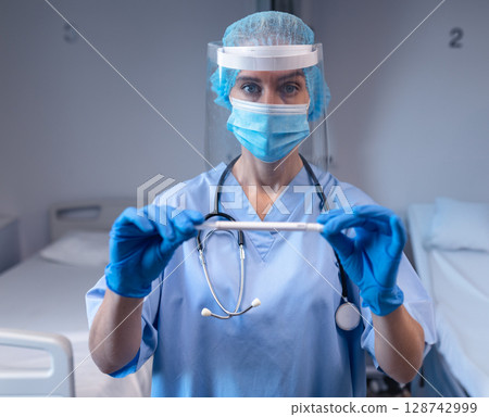 Nurse holding nasal swab in hospital ward bay, with stethoscope around neck and gloves 128742999