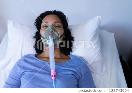 Young adult woman patient lying in hospital room on bed, wearing oxygen mask with clear tubing 128743004