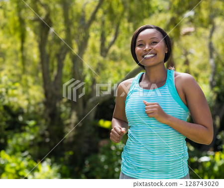 African American woman jogging in sunny park, with turquoise tank top and gray leggings, copy space African American woman jogging in sunny park, with turquoise tank top and gray leggings, copy space 128743020