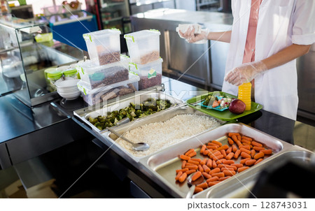 Asian woman assembling meal in cafeteria line on green tray, with apple, orange juice, copy space Asian woman assembling meal in cafeteria line on green tray, with apple, orange juice, copy space 128743031