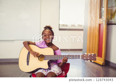 African American child sitting on red chair in class, playing acoustic guitar with whiteboard, map 128743043
