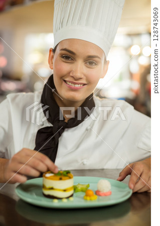 Female chef with tall hat garnishing plated dessert on mint-green plate in restaurant kitchen Female chef with tall hat garnishing plated dessert on mint-green plate in restaurant kitchen 128743069