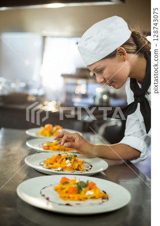 Asian female chef carefully garnishing pasta plates in commercial kitchen with tweezers, copy space Asian female chef carefully garnishing pasta plates in commercial kitchen with tweezers, copy space 128743075