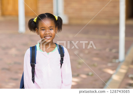 African American girl standing and smiling in brick school courtyard, carrying dark backpack 128743085