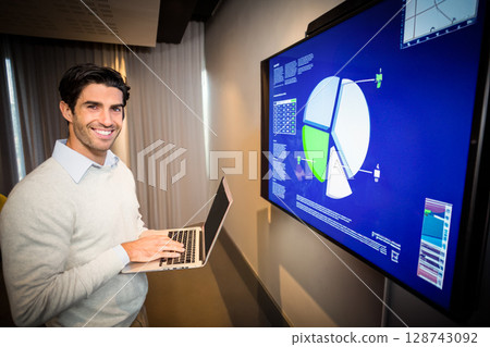 Man holding laptop and presenting pie chart data on wall display in modern office, copy space Man holding laptop and presenting pie chart data on wall display in modern office, copy space 128743092