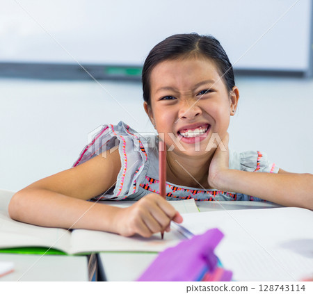 Asian girl child writing at school classroom desk with open notebooks, pencil and whiteboard behind Asian girl child writing at school classroom desk with open notebooks, pencil and whiteboard behind 128743114