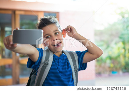 African American boy taking smartphone selfie at school entrance wearing backpack and playful face African American boy taking smartphone selfie at school entrance wearing backpack and playful face 128743116