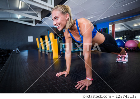 Mid-adult woman performing push-up in modern gym, with fitness tracker and kettlebells 128743132